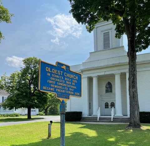 Sign in front of a church that says Oldest Church In Sennett Built 1820 Organized 1809 As First Congregational Remodeled 1847 Became Presbyterian 1870. 